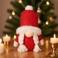 Gnomo navideño rojo con gorro de estrella y trenzas junto a un árbol iluminado - Gnomo hembra con chistera