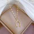 Collana a ferro di cavallo dorata con zirconi cubici su una scatola beige elegante - Stile Ferro di Cavallo Dorato (E121)