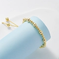 Detail of adjustable gold beaded bracelet on light blue pedestal with smooth metal texture - 4+6mm / Gold