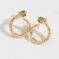 Macro shot of gold snake earrings with pink enamel details and green gemstone eyes - Pink