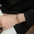 Dettaglio del bracciale rigido in metallo dorato intrecciato su modella con abito professionale - Stile 41 - Oro