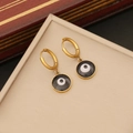 Golden hoop earrings with black evil eye pendants displayed on a beige leather pad - Evil Eye Gold Hoop Earrings