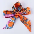 Orange twilly silk scarf with horse chain print tied in a neat bow on white background - S67-Orange Harness Chain