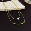 Detail view of a double-layered gold necklace featuring a white pearl and a textured metal tube - Gold Double Layered Necklace