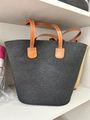 Black woven tote bag with brown faux leather handles displayed on a white shelf - Solid Black