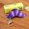 Purple gradient finger slug keychain with golden bell and packaging on wood surface - Purple