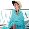 Teal blue Turkish beach towel with white stripes and fringe worn by a model poolside - Cyan