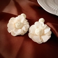 Detail von weißen Bastgewebe-Blumenohrringen auf einem edlen braunen Seidenhintergrund - Stud Ohrringe / Gebrochenes Weiß