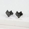 Detail view of black origami fox stud earrings on a textured white stone surface - 116 Fox / Black