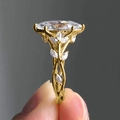 Detail showing marquise-cut crystal ring with golden vine and leaf design on grey background - Gold