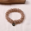 Detail of beaded champagne crystal hair tie with a round gold Morava engraved charm - Champagne