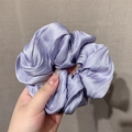 Satin scrunchie in lavender purple with glossy pleated texture held by a hand - Purple