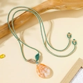 Close-up of a teardrop-shaped orange stone pendant on a woven green and beige cord - Pink Phantom Quartz Green/White Cord