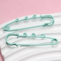 Detail of mint green multi-loop safety pins on a textured white pedestal base - Emerald Green