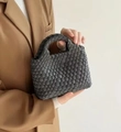 Close-up of a grey hand-woven bucket bag with a round handle held by a model - Gray