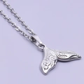Detailed close-up of a silver stainless steel whale tail pendant with engraved patterns - Necklace / Steel