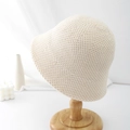 Detailed close-up of cream knit bucket hat texture on a wooden stand with elegant decor - Beige