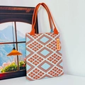 Detail of geometric knit tote bag with orange and blue diamond pattern and slogan tag - Diamond Grid Orange