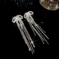 Detailed view of silver bow earrings with sparkling rhinestone tassels on dark background - Silver (925 Sterling Silver Earring Post)