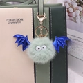 Detail eines grünen Kunstpelz-Fledermaus-Anhängers mit blauen Glitzerflügeln an der Tasche - Goldene Kette / Minzgrün & Königsblaue Flügel