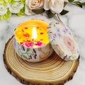 Candela profumata in latta floreale con petali essiccati e fiamma accesa su legno - Camomilla