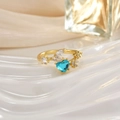 Macro shot of a golden heart ring featuring a blue gemstone and small zircon accents - Blue Heart Beads Rhinestone Style (JZ0152B)