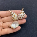 Close-up of hand holding natural seashell pendants with brown spots and gold plated edges - No.14 (Brown Spotted Conch - Gold Edge)