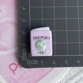 Macro shot of purple resin passport charm with earth illustration and passport text detail - Purple Travel Guide Book