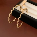 Vista macro di orecchini a cerchio ondulati placcati in oro su confezione regalo - Oro (Placcato Oro Vero)