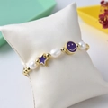 Vue macro d'un bracelet en perles d'eau douce avec charms étoile et smiley violets - Violet/Or