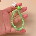 Detailed shot of green iridescent beads with matching bell and white clip on a phone charm - Green
