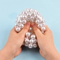 Gros plan de mains pressant une balle anti-stress transparente avec des perles blanches - Perle Colorée / 8cm