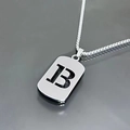 Detail of silver hollow letter B pendant on a box chain over a reflective surface - Letter B