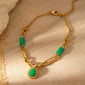 Detailaufnahme des Goldarmbands mit grünen Steinanhängern auf sandigem Stein-Hintergrund - Grünes Jadelook Tropfenarmband (LC40039)