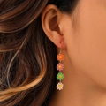 Detalle de pendientes de margaritas coloridas usados por una modelo con estilo floral vivo - Pendientes de flores coloridas