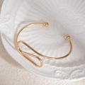 Vue détaillée d'un bracelet ouvert en spirale dorée sur une assiette en céramique - Bracelet manchette à boucle profilée à double boule dorée