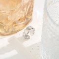 Detailaufnahme eines silbernen Herz-Gliederrings aus Edelstahl auf weißem Stein - Unregelmäßiges Herz Silber