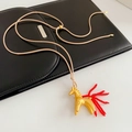 Detailaufnahme eines goldenen Pferdeanhängers mit rotem Perlenschwanz an Kordel - Matt Gold