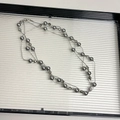 Sautoir multicouche avec perles grises et chaînes argentées sur un plateau blanc - Collier de perles grises