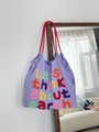 Detail of purple canvas tote bag with embroidered letters and red woven handles - Purple