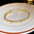 Macro shot of gold plated open cuff bracelet with white zircon on striped white ceramic - Gold (Real Gold Plated)