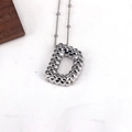 Macro detail of silver necklace featuring a textured letter D pendant with rivet patterns - Letter D