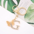 Detailed view of a gold letter G keychain with sparkling crystals and a hollow butterfly charm - Letter G