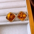 Close-up of amber resin square earrings with gold metal frame on a textured jewelry box - Silver Needle / Gold Brown Square
