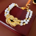 Dettaglio di una collana di perle a doppio strato con nodo dorato su legno scuro - Collana - Oro - Bianco