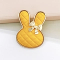Macro detail of yellow bunny charm with quilted texture and golden metal accents - Turmeric