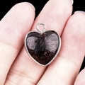 Natural black obsidian heart pendant with silver bezel frame shown in hand - Fireworks Stone Silver Edging