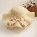 Close-up of beige straw hat featuring wavy brim and elegant fabric bow decoration - One Size / Beige