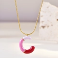 Detailopname van gouden letter C-hanger met roze en rood emaille aan een ketting - Letter C