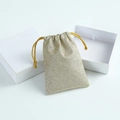 Close-up of glitter gold drawstring jewelry pouch and premium white gift box on clean background - Beige